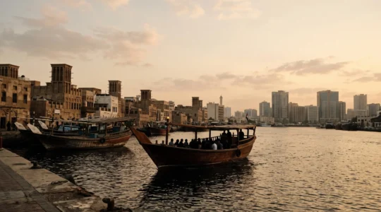 Bateau en bois traditionnel abra glissant sur le Dubai Creek au coucher du soleil, entre le vieux souk et les tours modernes